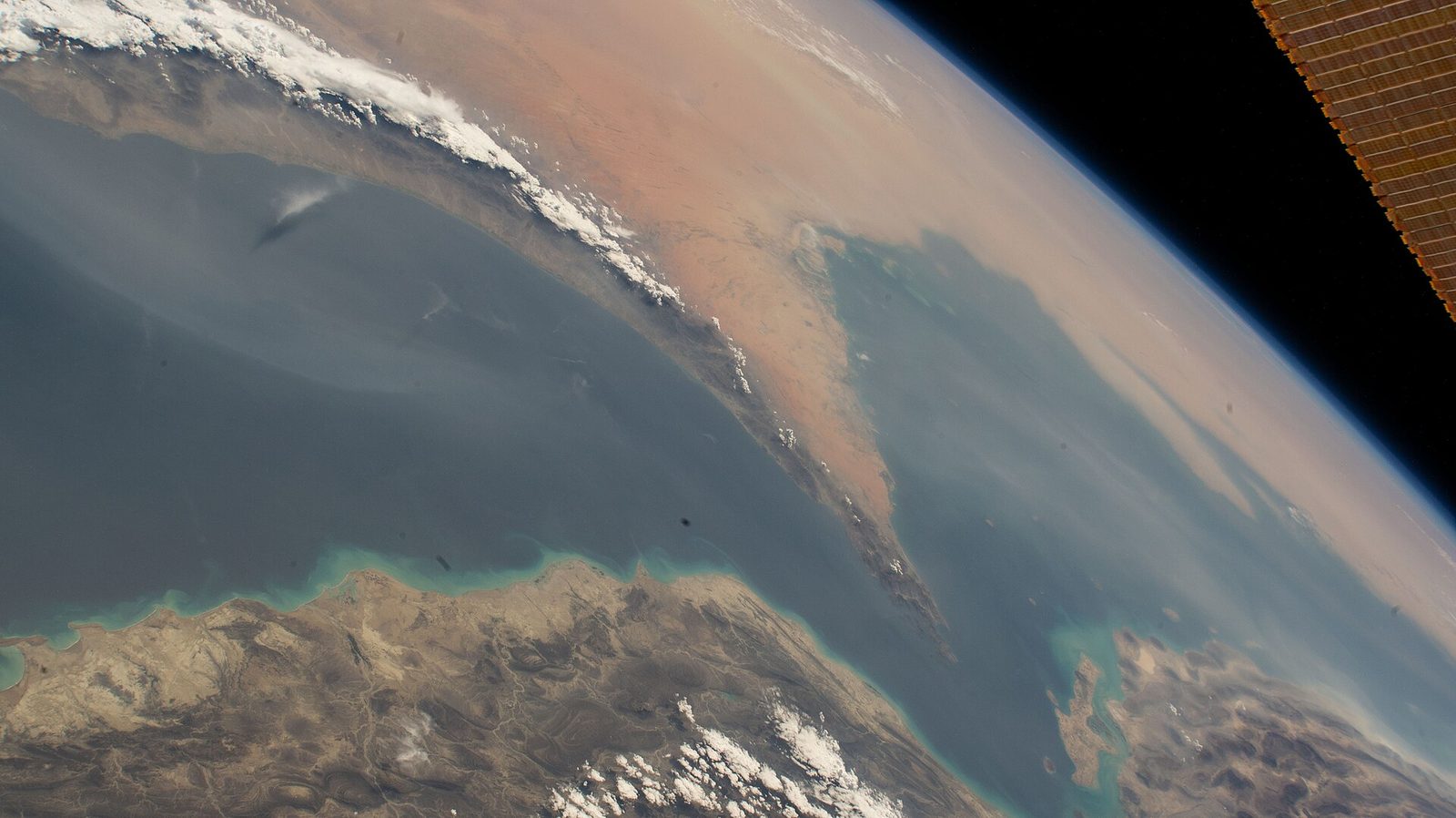 Photograph from the International Space Station looking down on the Strait of Hormuz: the Musandam Peninsula of Oman juts up from the bottom of the frame toward the Iranian coast, with the Persian Gulf on the left and the Gulf of Oman on the right, the Earth's curve and the blackness of space at the top right